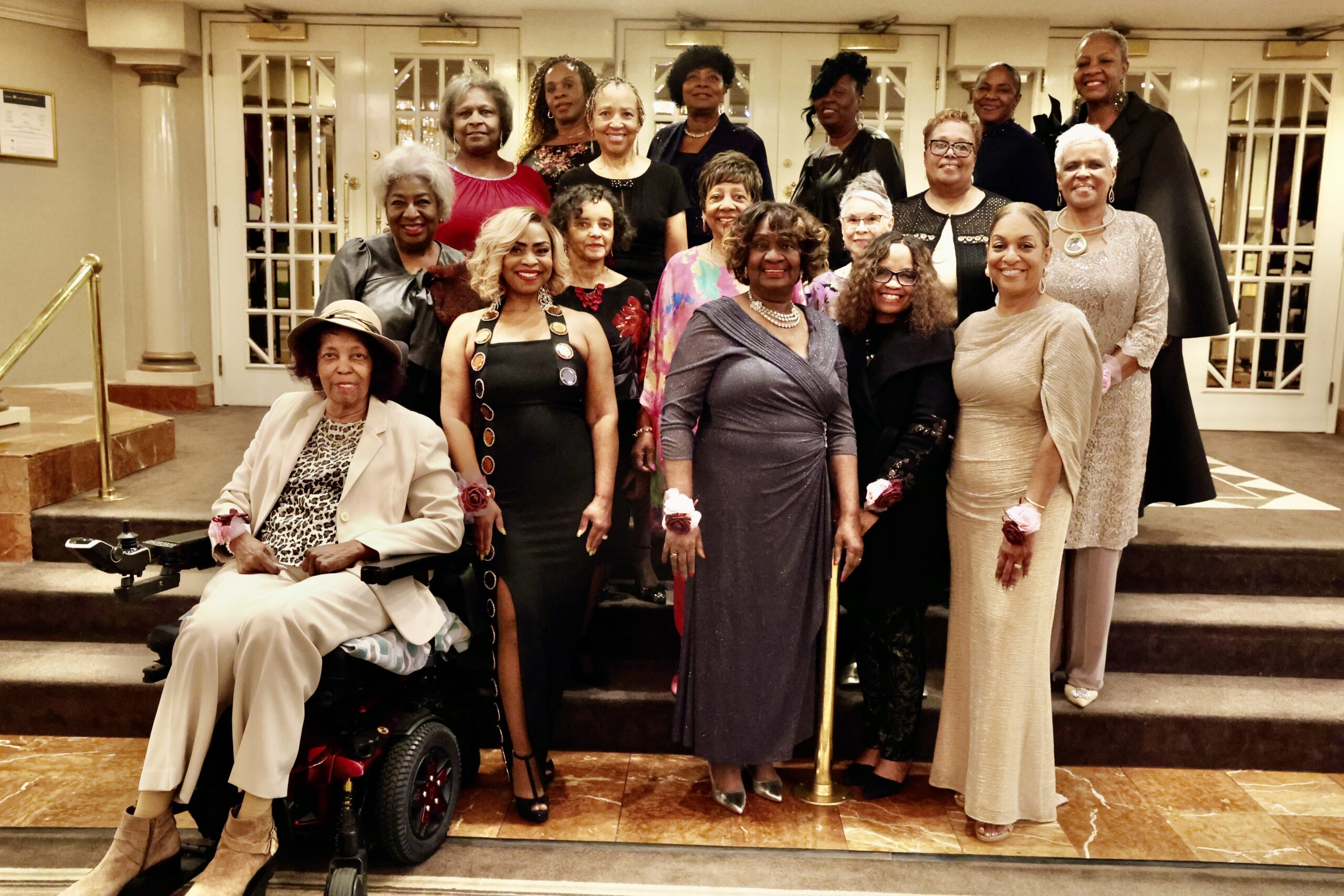 A celebratory group of women in elegant attire poses together indoors, showcasing a sense of community and empowerment at a formal event.